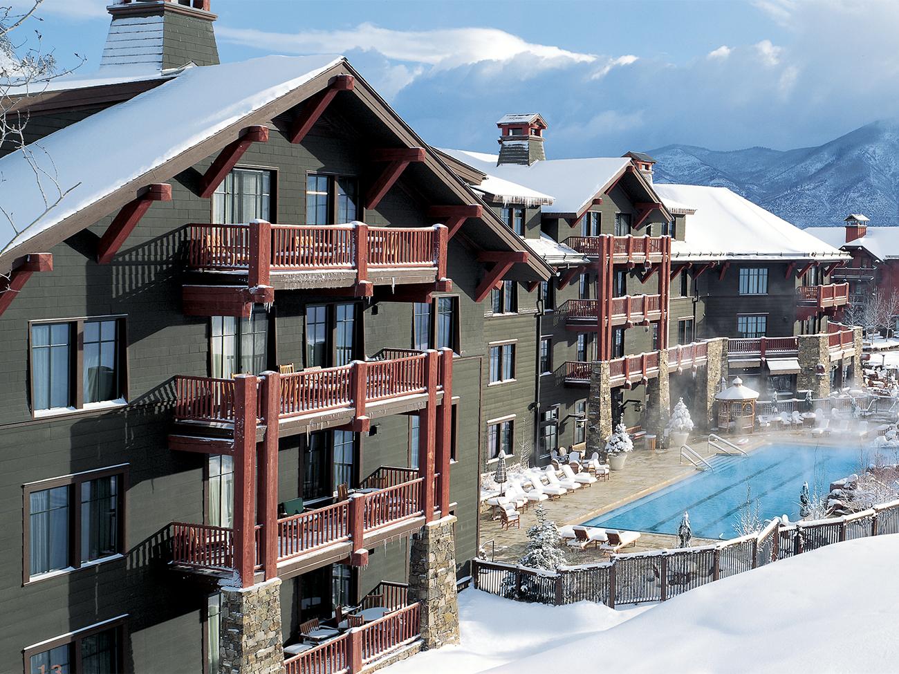 Exterior of The Ritz-Carlton Club Aspen Highlands resort timeshare showing snow-covered grounds and steam rising from pool