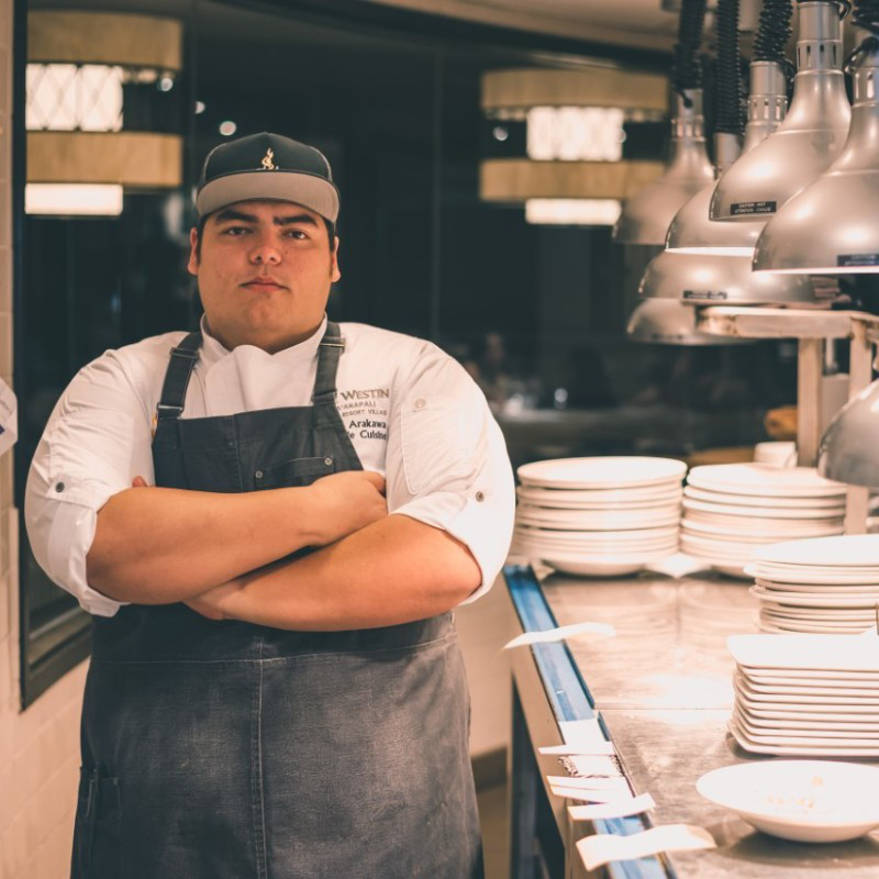 A chef with an apron stands next to a long table with many plates