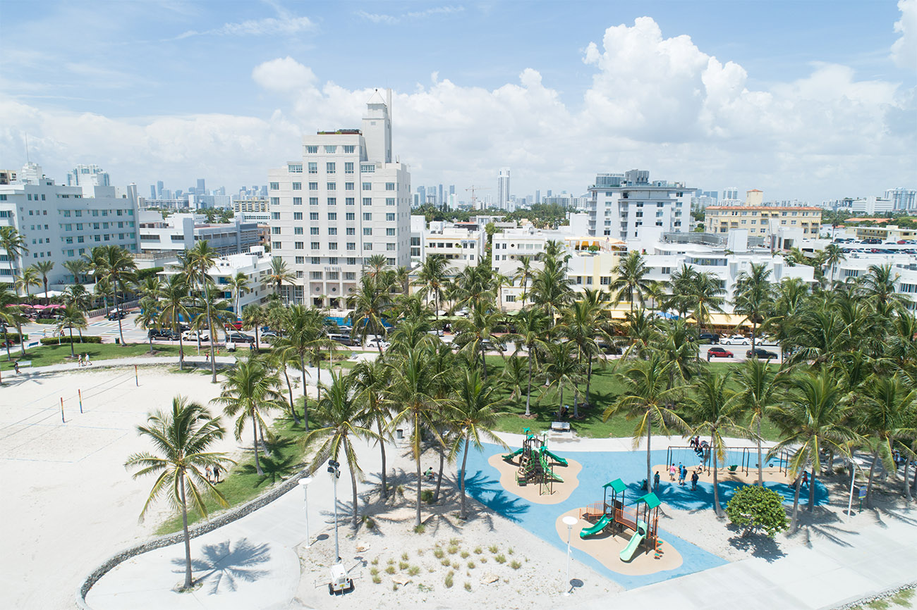 Palm trees provide shade for an outdoor playground surrounded by white sand.