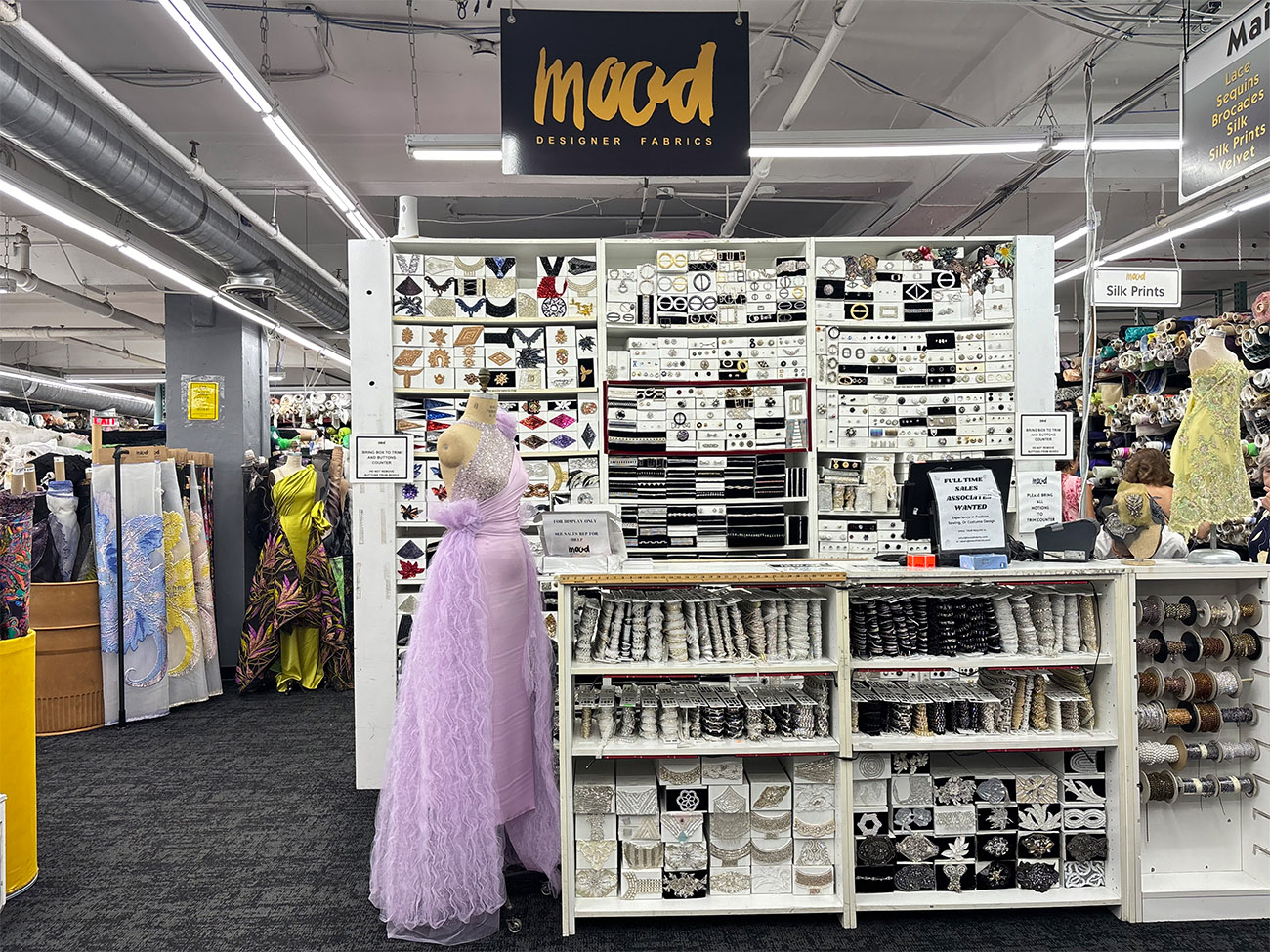 A large display of fabrics sits on a shelf behind a mannequin 