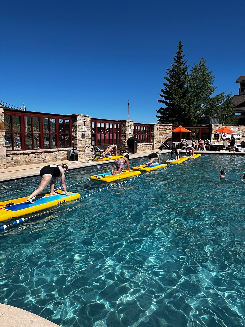 A group of guests strike a yoga pose on floaties in the middle of a pool