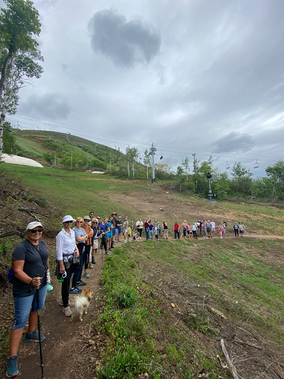 A line of people hike on a well-maintained trail in the grass