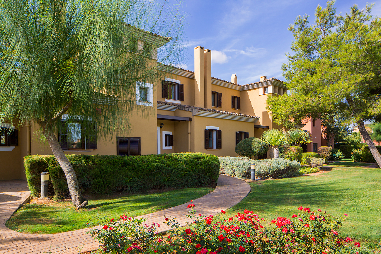 A foliage-lined path leads to the entrance of a Spanish building
