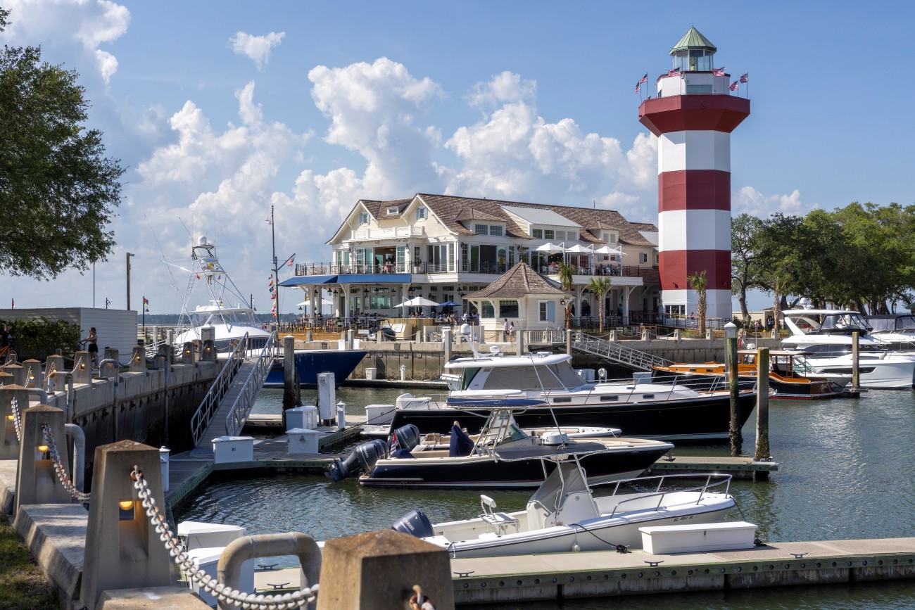 4. A series of boats sits in a harbor with a lighthouse and restaurant just off the shore.