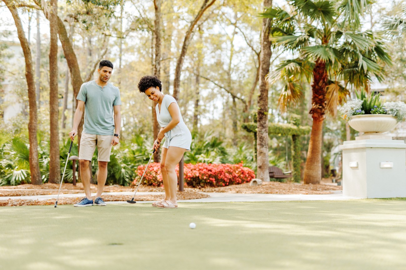 5. A couple play mini golf surrounded by palm trees and flowers.