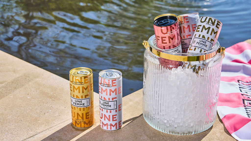 2) A cooler with cans of Une Femme sparkling wine on a striped towel.