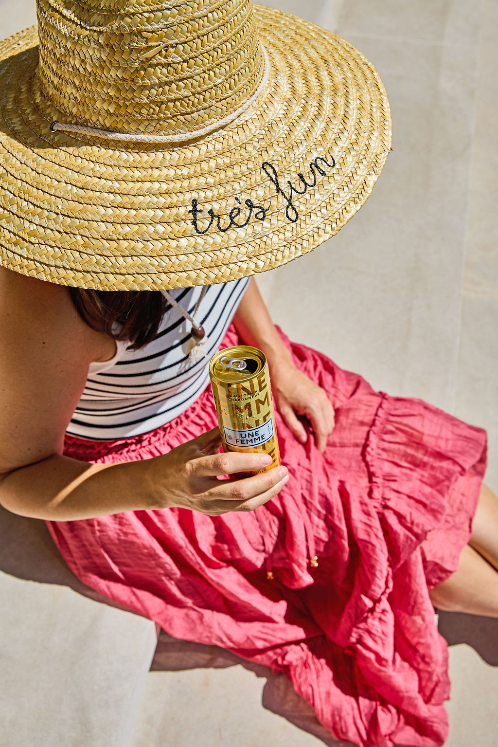 A woman in a wide-brimmed hat with the words “très fun" on it holds a can of Une Femme wine