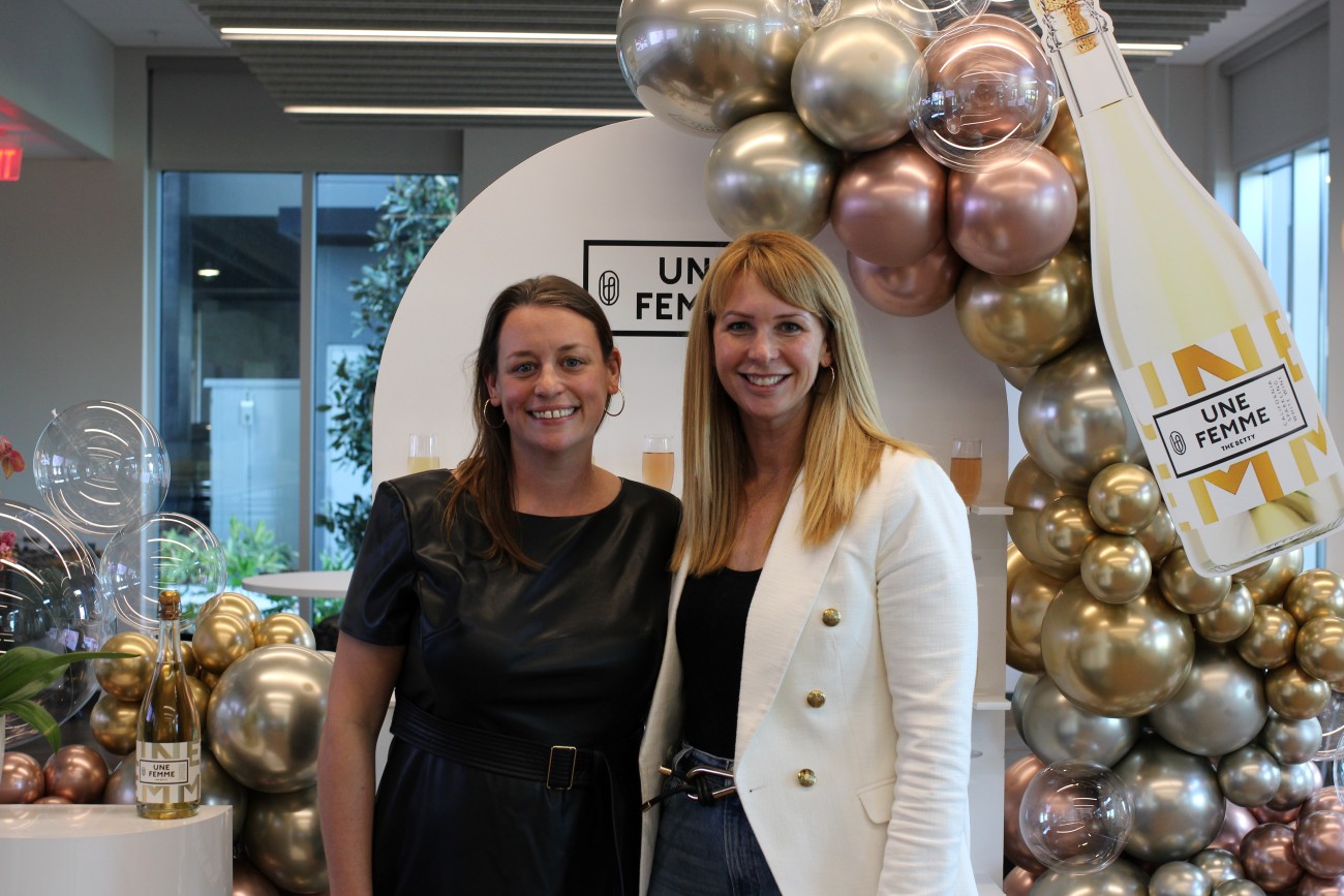 1) Jen Pelka and Lori Gustafson stand in front of a floral backdrop for Une Femme.