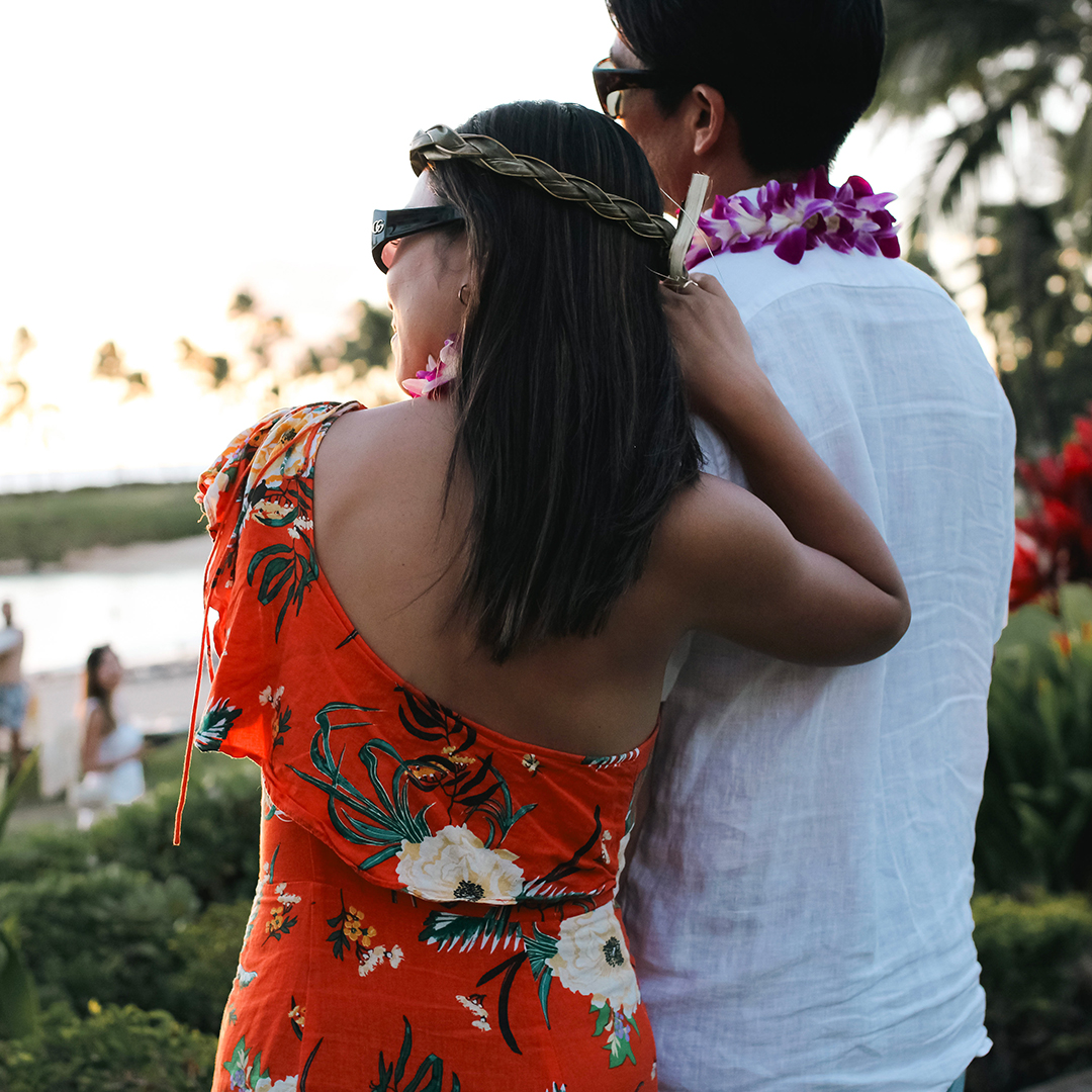 A man and woman in Hawaiian clothes look out over the lagoon at sunset.