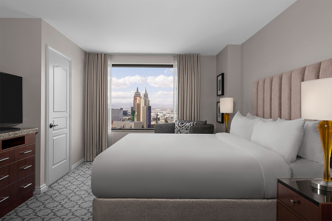 A comfortable bed sits in a well-adorned villa with the Strip showing out of the window.