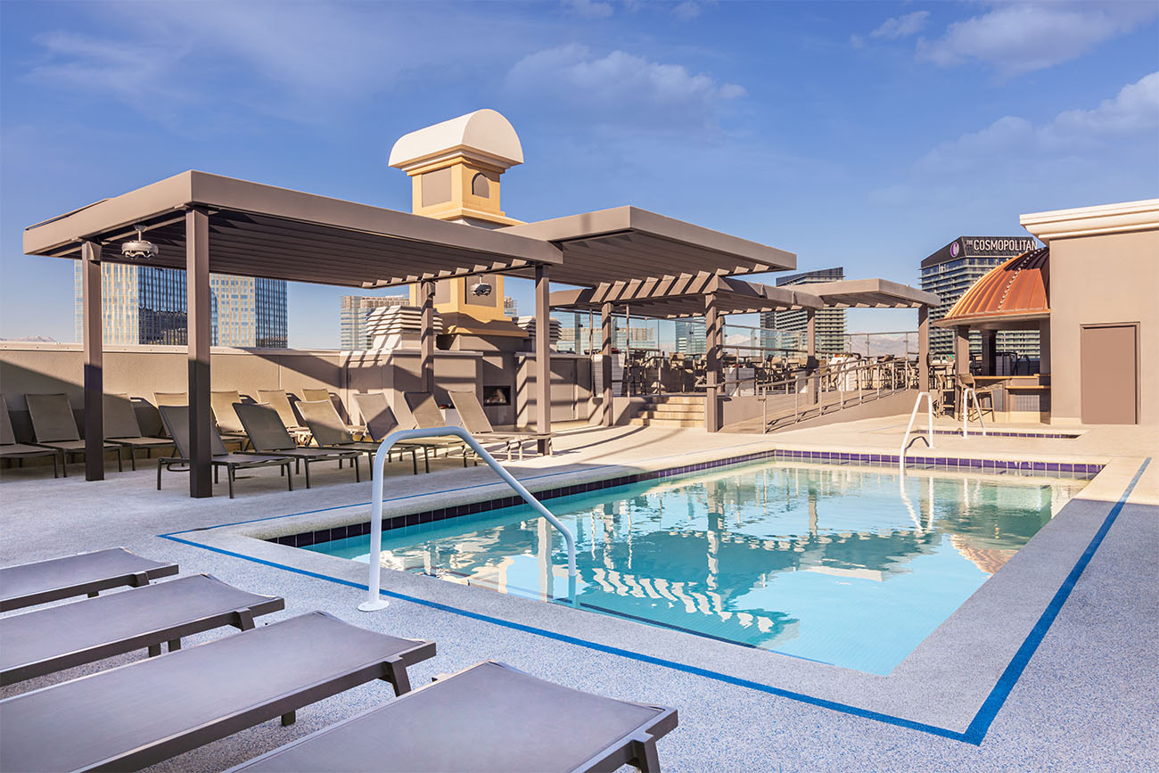 A rooftop pool is surrounded by patio furniture underneath a clear Vegas sky.