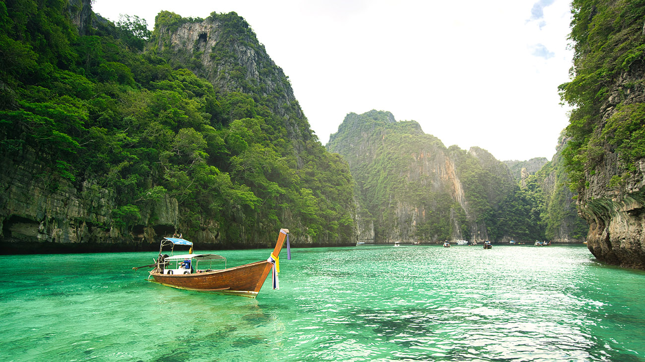 A boat and its passenger sit on the calm, clear waters of the ocean as it cuts through natural rock formations.