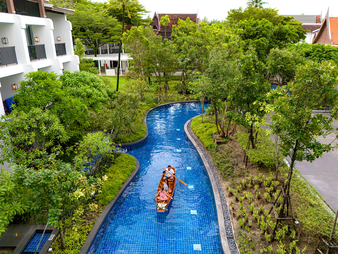 Guests sit in a small gondola and are floating down a tree-lined waterway going to check in.