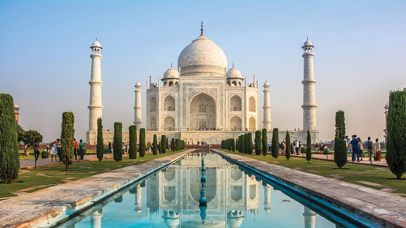 Taj Mahal in Agra with its reflection in a long pool and a bright blue sky.