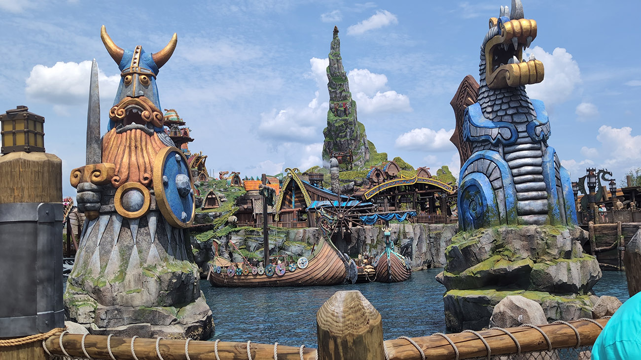 Video thumbnail showing a person walking through a theme park area with trees and signage in the background.