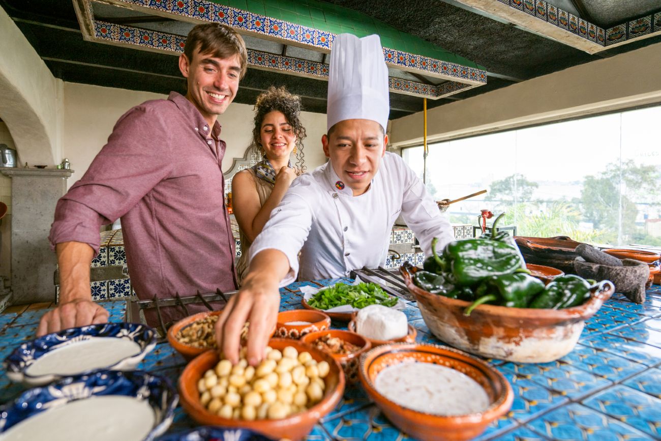 A chef and guests stand beside a table filled with fresh ingredients.