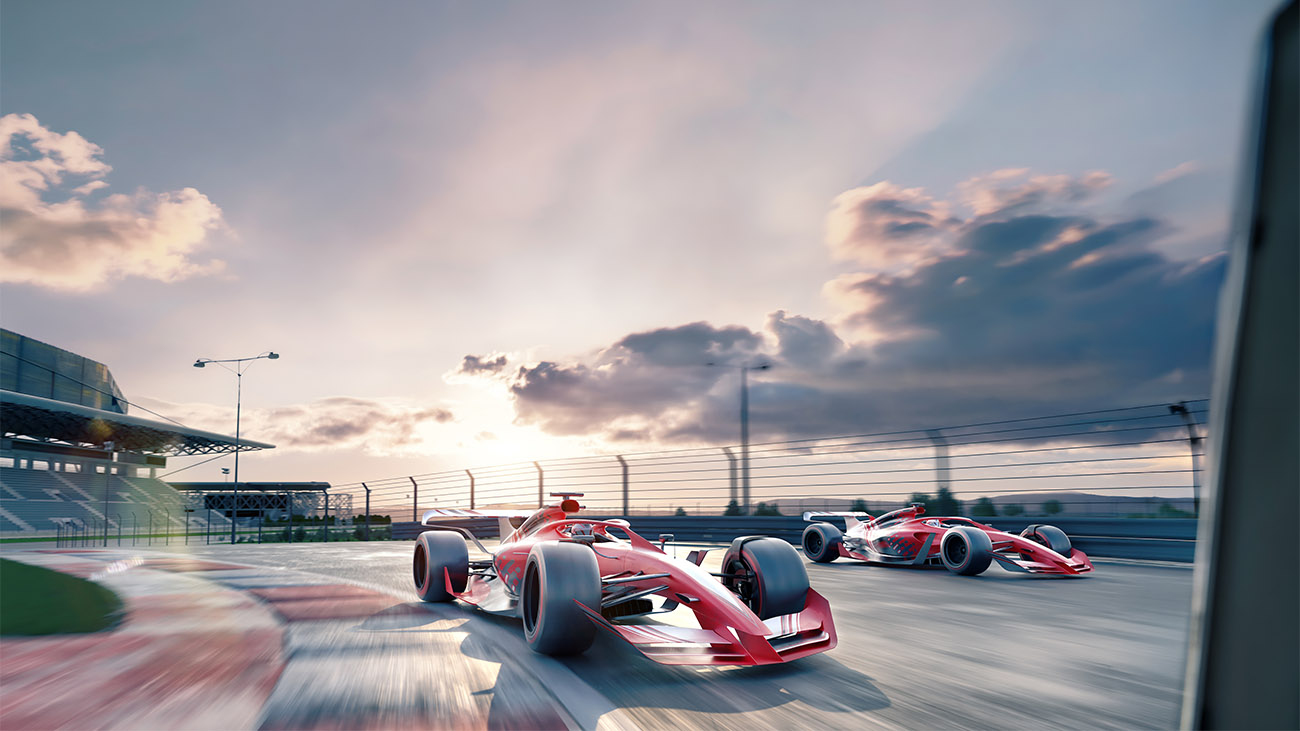 Sports cars line up on a racetrack under a cloudy sky.