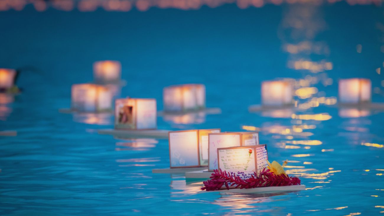 Glowing lanterns float across calm water during a nighttime celebration.