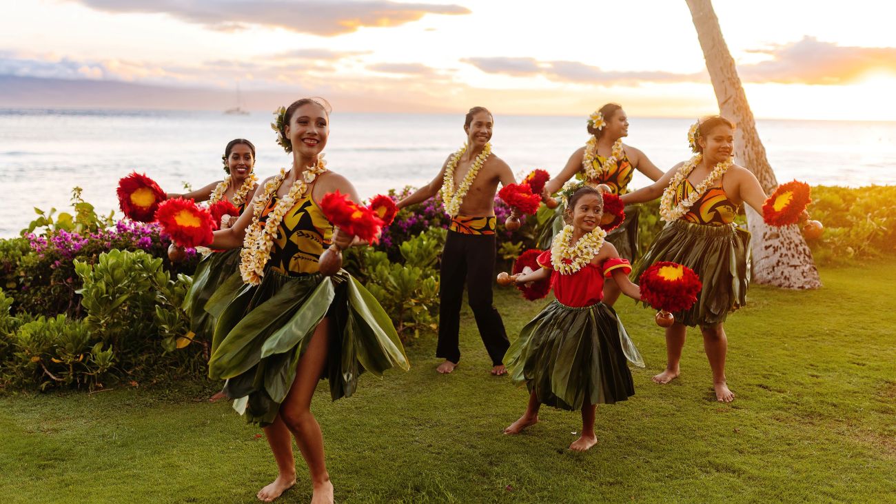 A group of performers in traditional Hawaiian clothing dances hula.